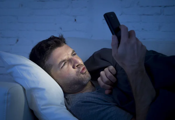 Man in bed couch at home late at night using mobile phone in low light watching online porn