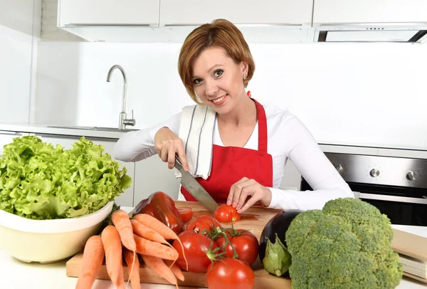 Happy woman at home kitchen preparing vegetable salad with lettuce, carrots and slicing tomato smiling