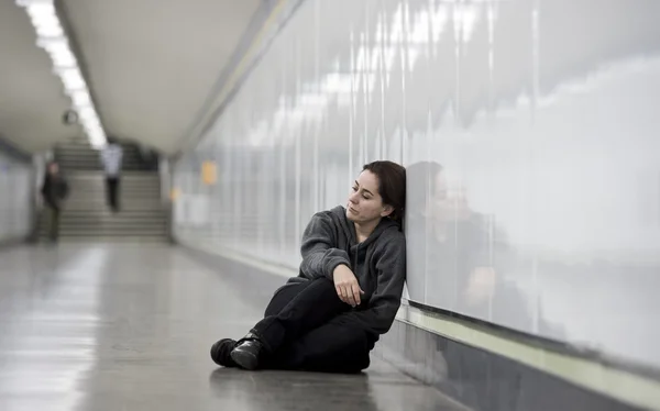 Young sad woman in pain alone and depressed at urban subway tunnel ground worried suffering depression