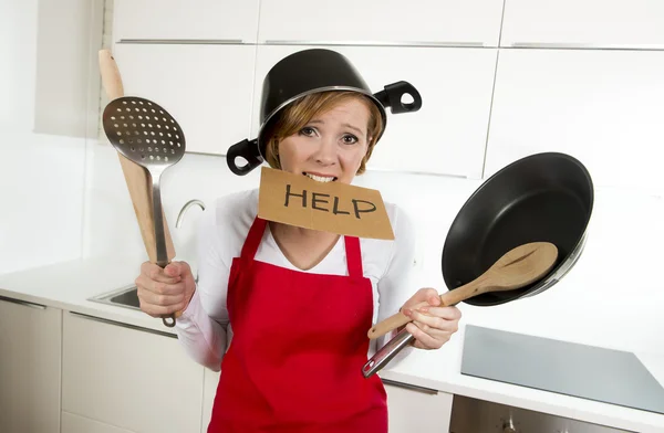 Young attractive home cook woman in red apron at  kitchen holding pan and household with pot on her head in stress