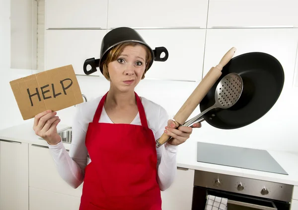 Young attractive home cook woman in red apron at  kitchen holding pan and household with pot on her head in stress