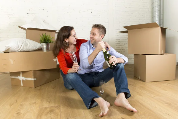Happy couple sitting on floor unpacking together celebrating with champagne toast moving in new house