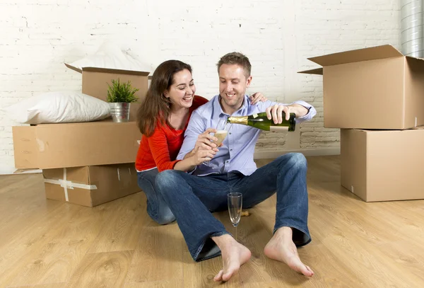 Happy American couple sitting on floor unpacking together celebrating with champagne toast moving in a new house