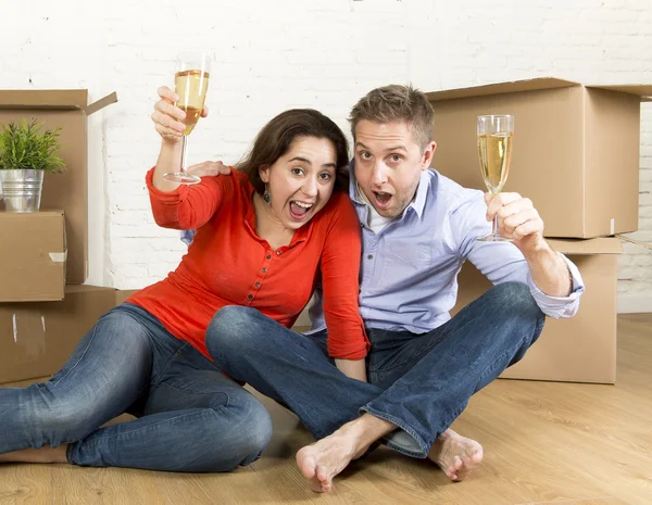 Happy American couple sitting on floor unpacking together celebrating with champagne toast moving in a new house