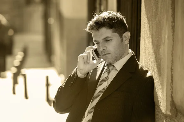 Young attractive and busy businessman with blue eyes wearing suit and tie talking business on mobile phone outdoors