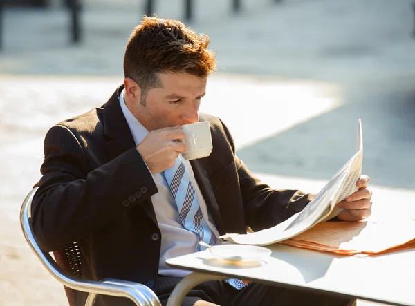 Attractive businessman sitting outdoors having coffee cup for breakfast early morning reading newspaper news looking relaxed