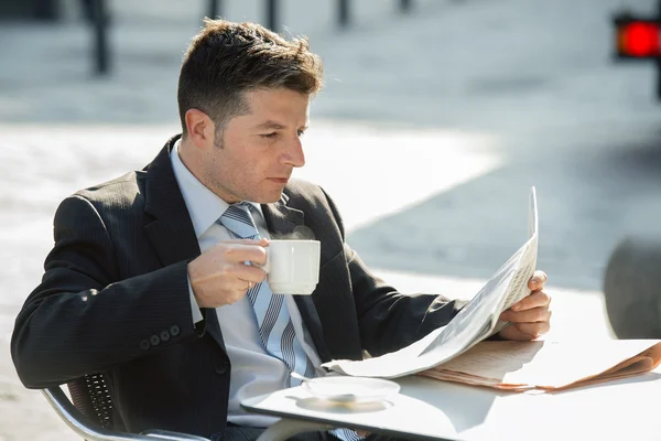 Attractive businessman sitting outdoors having coffee cup for breakfast early morning reading newspaper news looking relaxed