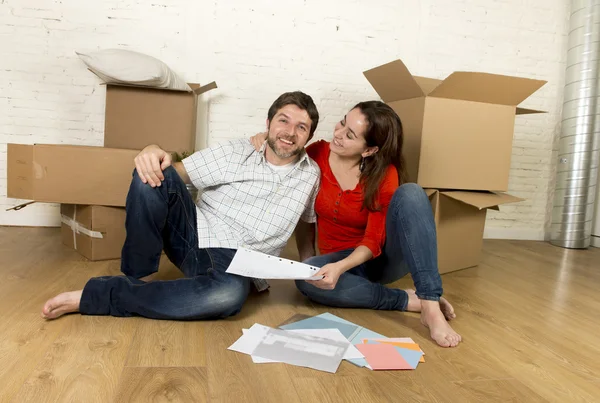Happy American couple sitting on floor moving in new house looking blueprints