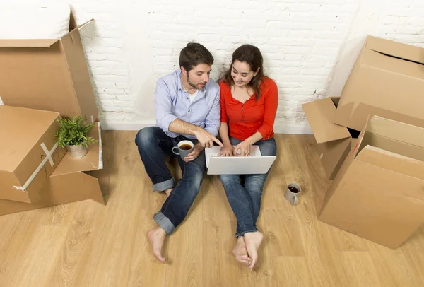 Couple sitting on floor moving in new house choosing furniture with computer laptop