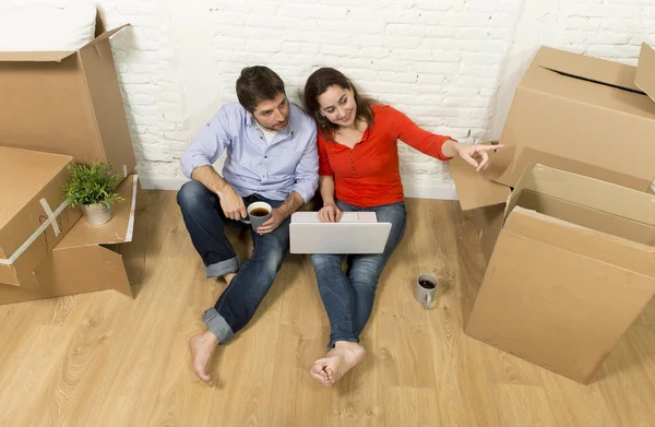 Couple sitting on floor moving in new house choosing furniture with computer laptop