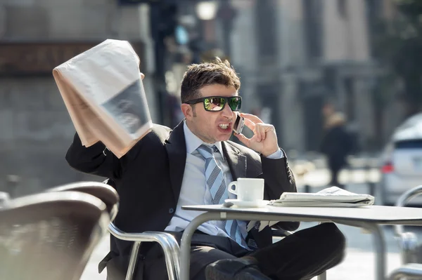 Businessman holding newspaper angry and upset as if reading bad news  talking on mobile phone