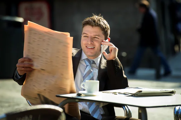 Businessman on street bar having breakfast coffee reading newspaper news talking on mobile phone