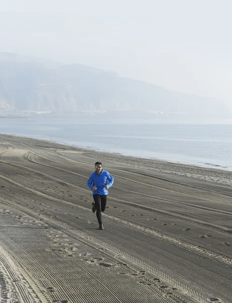 Young sport man running alone on desert beach along the sea shore training workout