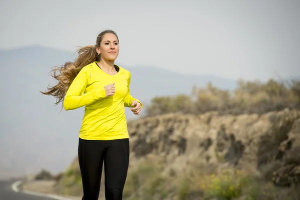 Young attractive sport woman running on asphalt road with desert mountain landscape background