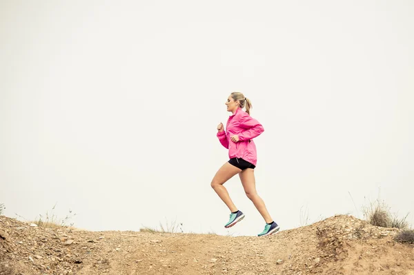 Young sport woman running off road trail dirty road with dry desert landscape background training hard