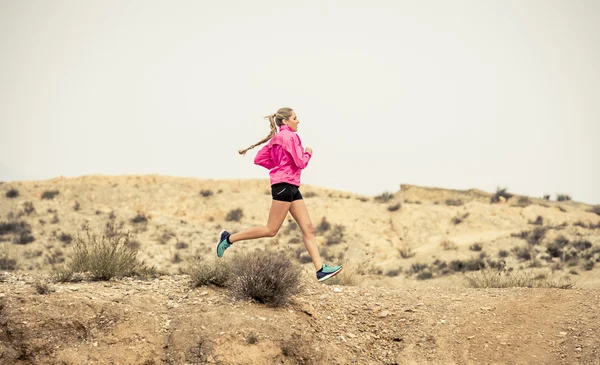 Young sport woman running off road trail dirty road with dry desert landscape background training hard