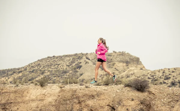 Young sport woman running off road trail dirty road with dry desert landscape background training hard