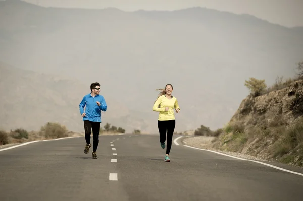 Attractive sport couple man and woman running together on asphalt road mountain landscape