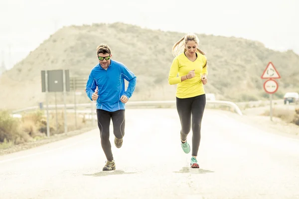 Attractive sport couple man and woman running together on asphalt road mountain landscape