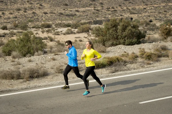 Attractive sport couple man and woman running together on desert asphalt road mountain landscape