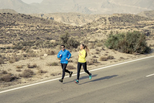 Attractive sport couple man and woman running together on desert asphalt road mountain landscape