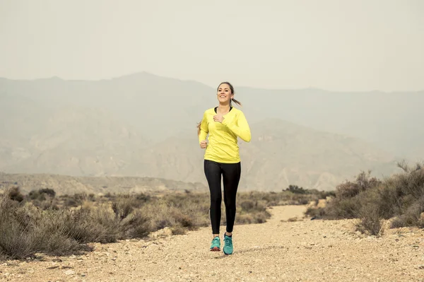 Attractive sport woman running on earth trail dirty road with desert mountain landscape