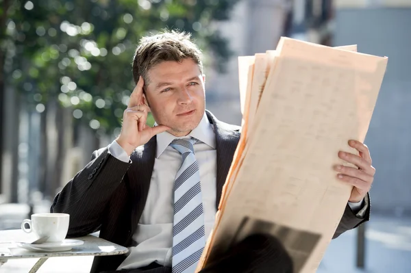 Attractive businessman sitting outdoors having coffee cup for breakfast early morning reading newspaper news looking relaxed