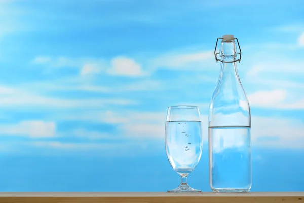 Fresh and clean drinking water in bottle and glass on sky background