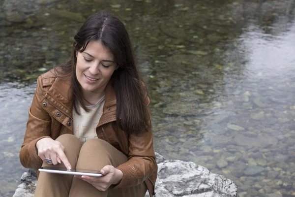 Sitting on a rock by the water and using a digital tablet