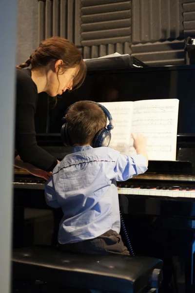 Rear view of a little boy learning piano from female instructor