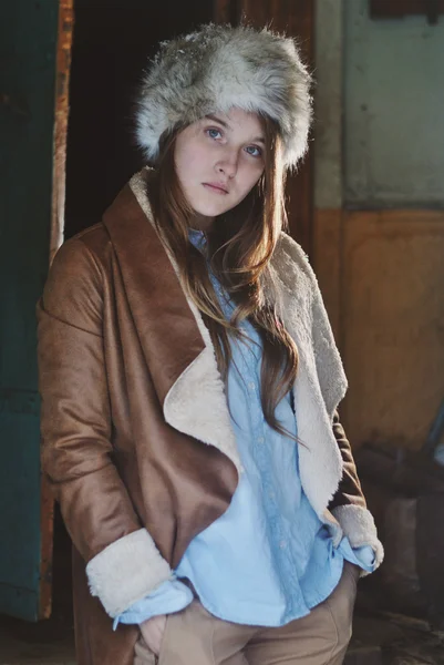 Autumn portrait photo of posing pretty model girl wearing fur hat and leather coat standing in doorway