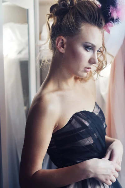 Portrait photo of beautiful girl standing looking at window wearing dress and feather hair