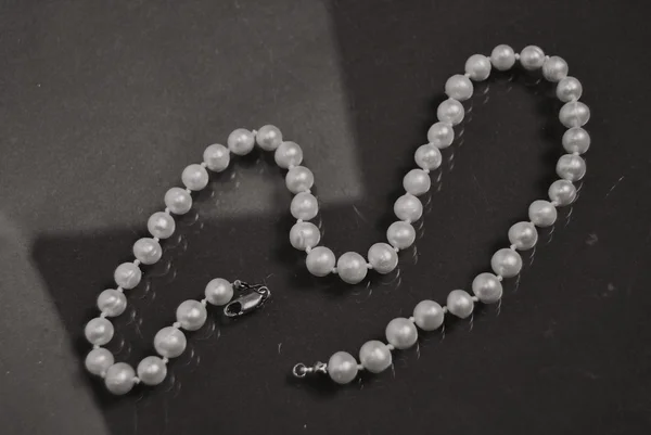 Pearl necklace lying on grey and black background. black and white monochrome photo