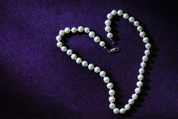 Pearl beads in heart shape on purple velvet background