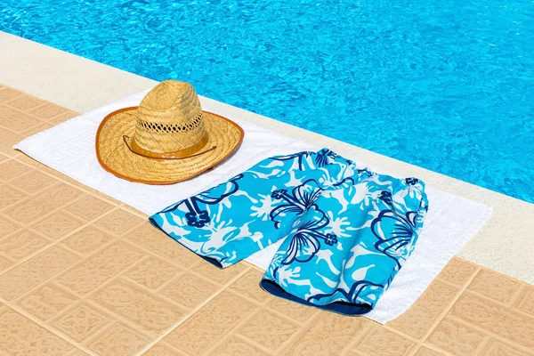 Hat and swimming trunks on towel near swimming pool