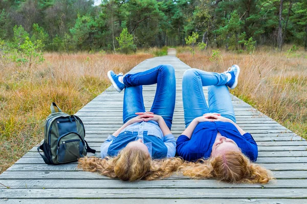 Two girls lying on their backs on path in nature