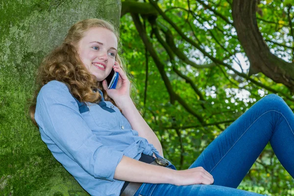 Dutch teenage girl phoning mobile in green tree