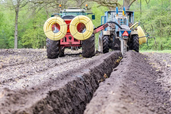 Two agriculture tractors putting drainage pipes in ground