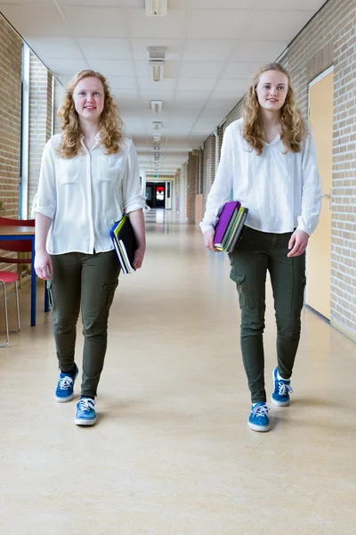 Two dutch teenage girls walking in long school corridor carrying