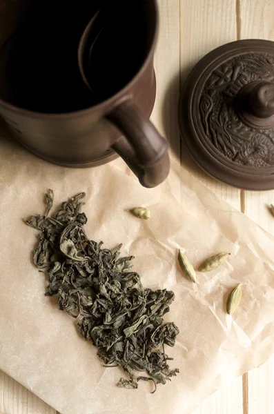 Clay cup with lying next to green tea and cardamom