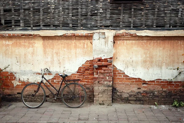 An old, rusty white bicycle with a basket leaning against a grungy wall in Italy.