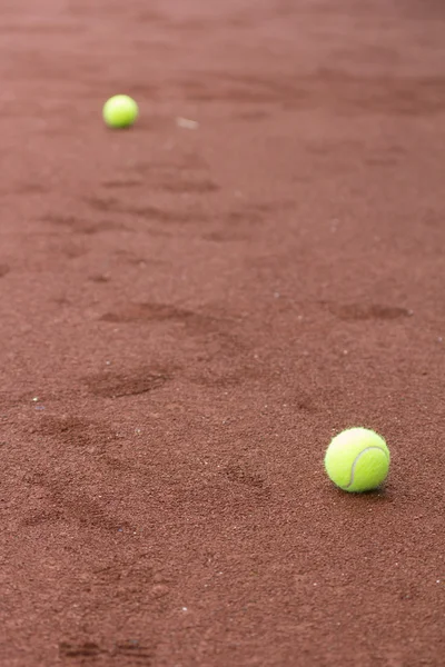 Two green tennis balls on the clay court