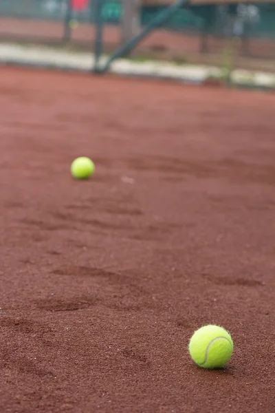 Two green tennis balls on the clay court
