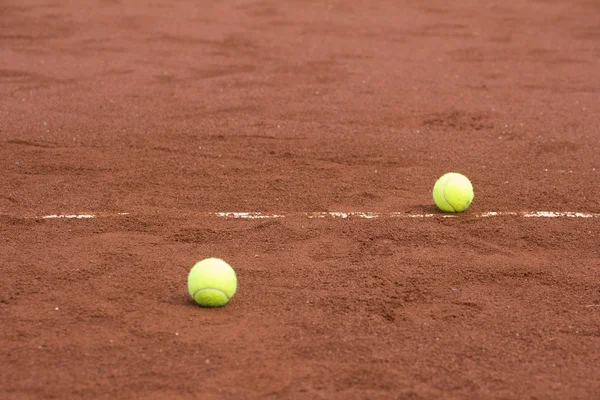 Two green tennis balls on the clay court