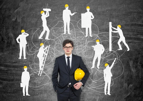 Businessman with yellow helmet, silhouettes of businessmen with different construction tasks around him, Black background. Concept of business construction.