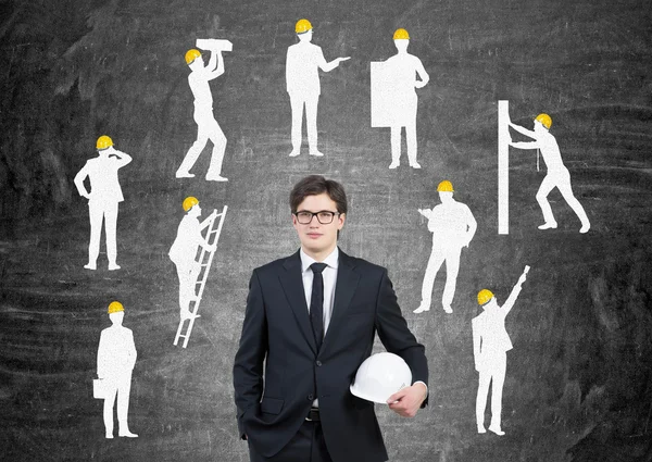 Businessman with white helmet, silhouettes of businessmen with different construction tasks around him, Black background. Concept of business construction.