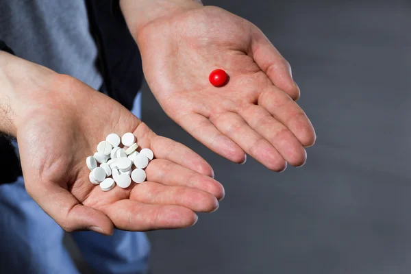 Man with pile of white pills in one hand and a red pill in another