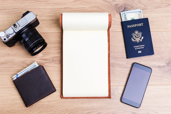 Traveling concept with blank notepad, camera, purse, american passport and blank smart phone on wooden desktop. Mock up