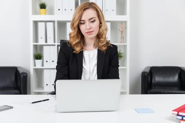 Businesswoman with wavy hair wearing suit working with her laptop in office. Concept of entrepreneurship