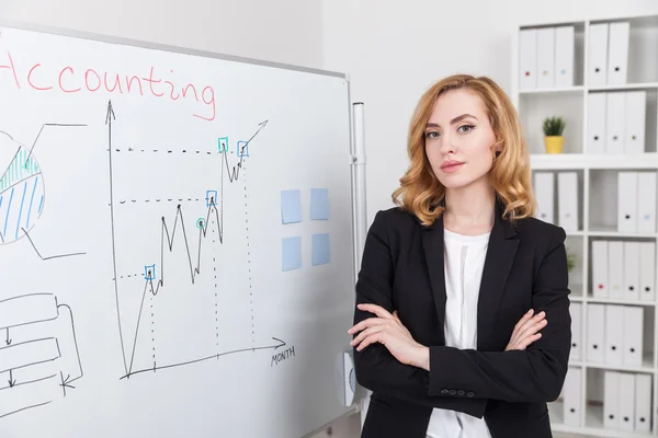 Content woman with her hands folded standing near whiteboard looking to camera. Concept of job well done